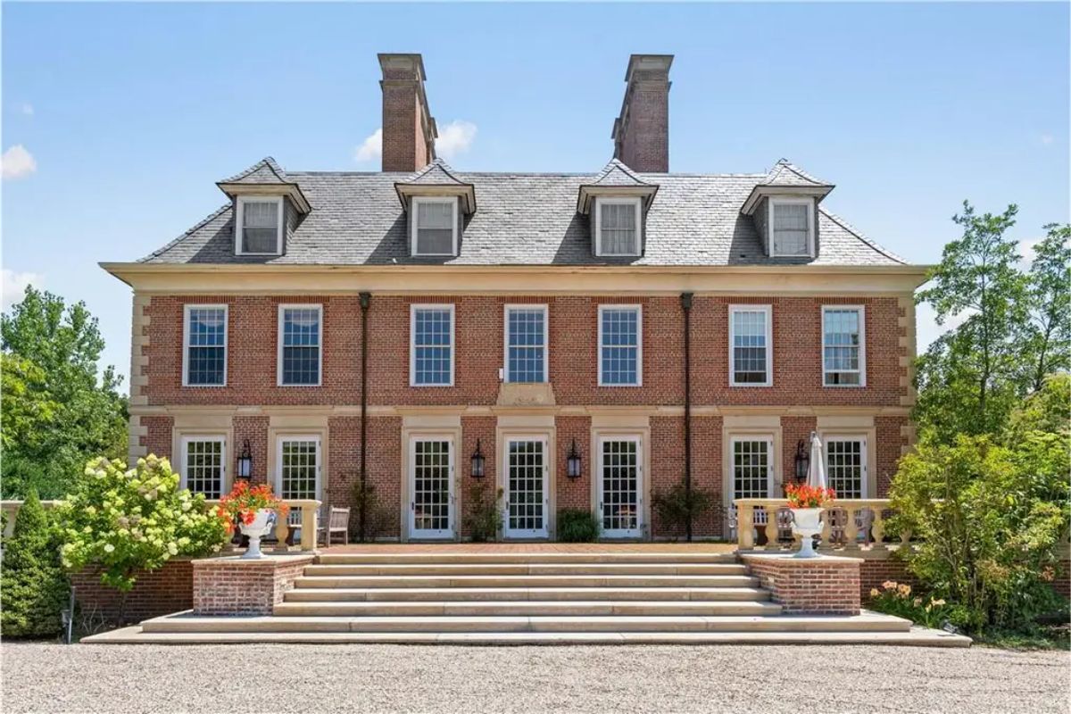 Grand front facade of a three-story Georgian-style mansion featuring brick walls and symmetrical design elements. 