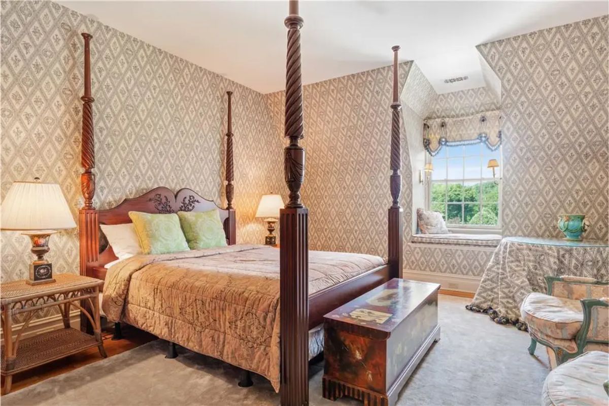 Elegant bedroom with a four-poster bed, patterned wallpaper, and a cozy seating area by the window. 