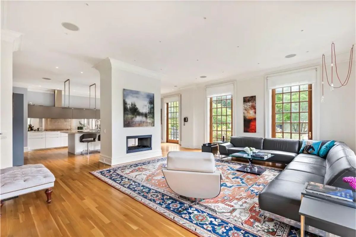 Spacious modern living area with a sleek fireplace, large sectional sofa, and natural lighting through tall windows. 