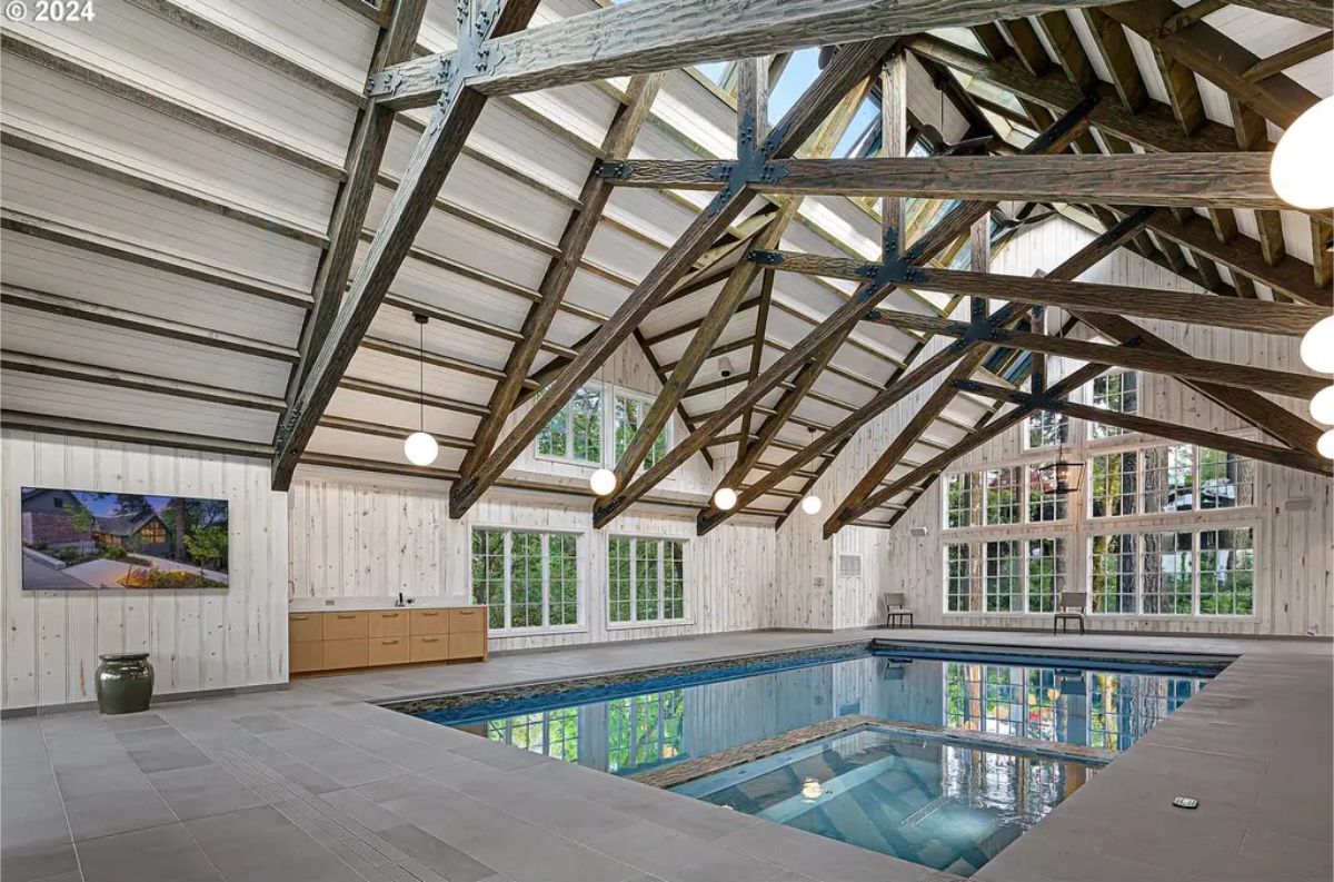 Indoor pool room boasts a vaulted ceiling with exposed wood beams and skylights.