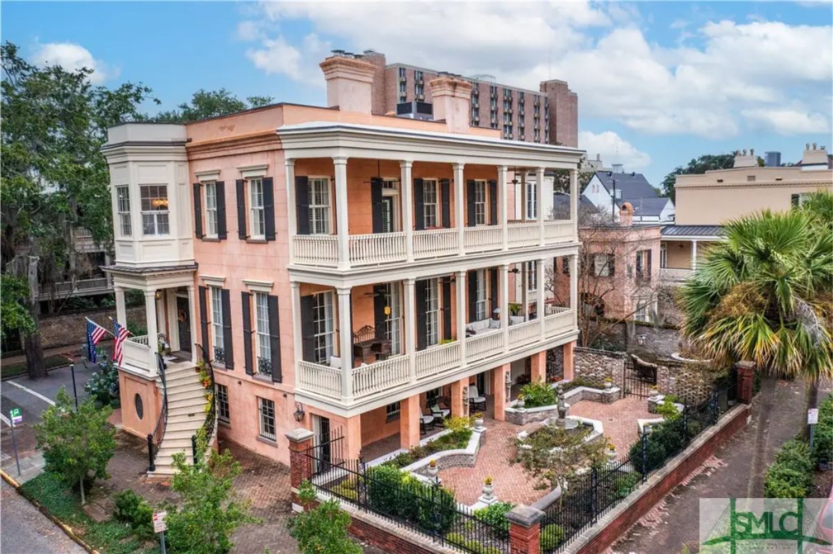 The three-story Southern mansion showcases a classic peach-colored exterior with triple wraparound porches.