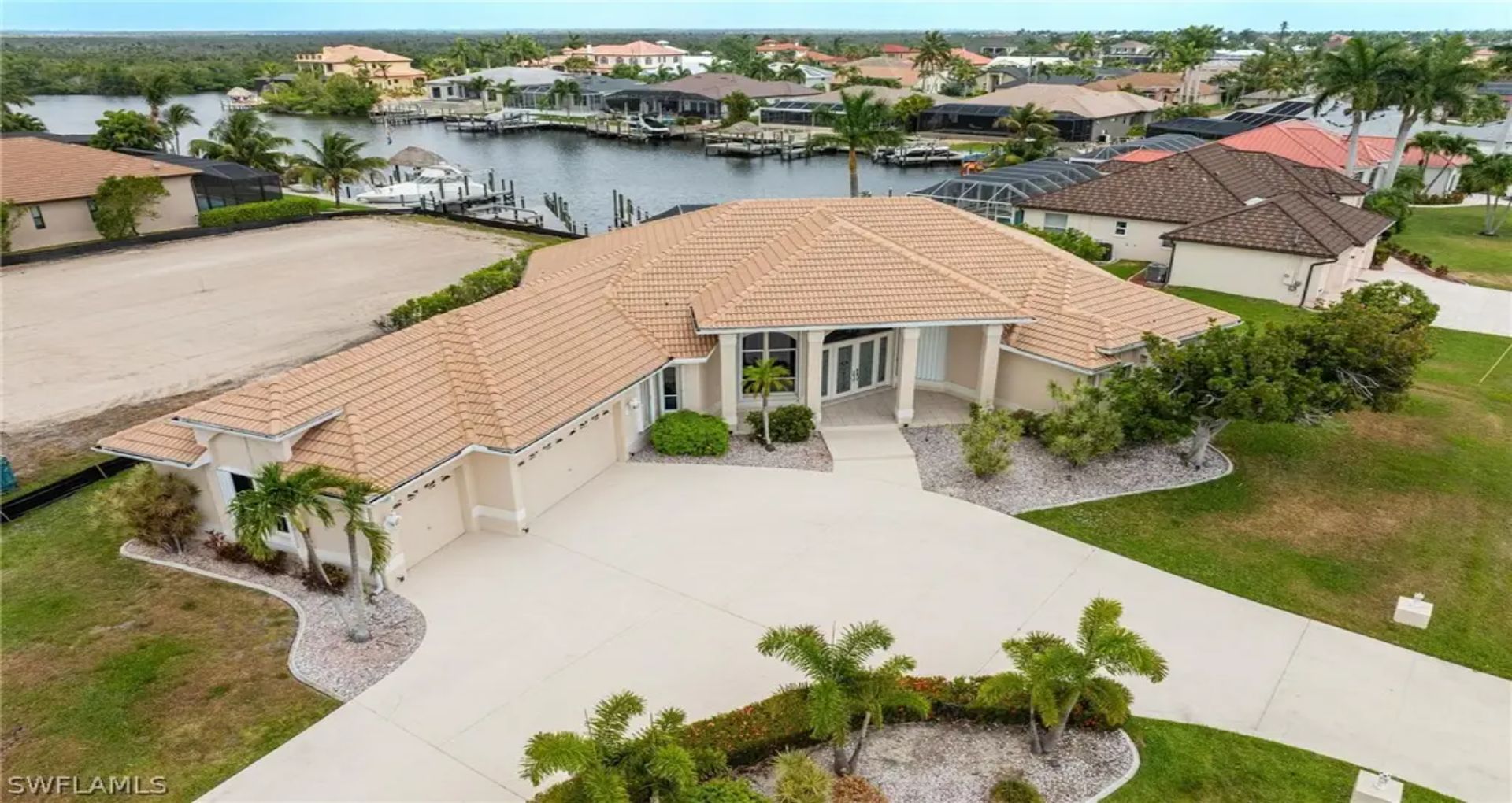 A single-story home with a tile roof and light stucco exterior sits on a spacious waterfront lot.