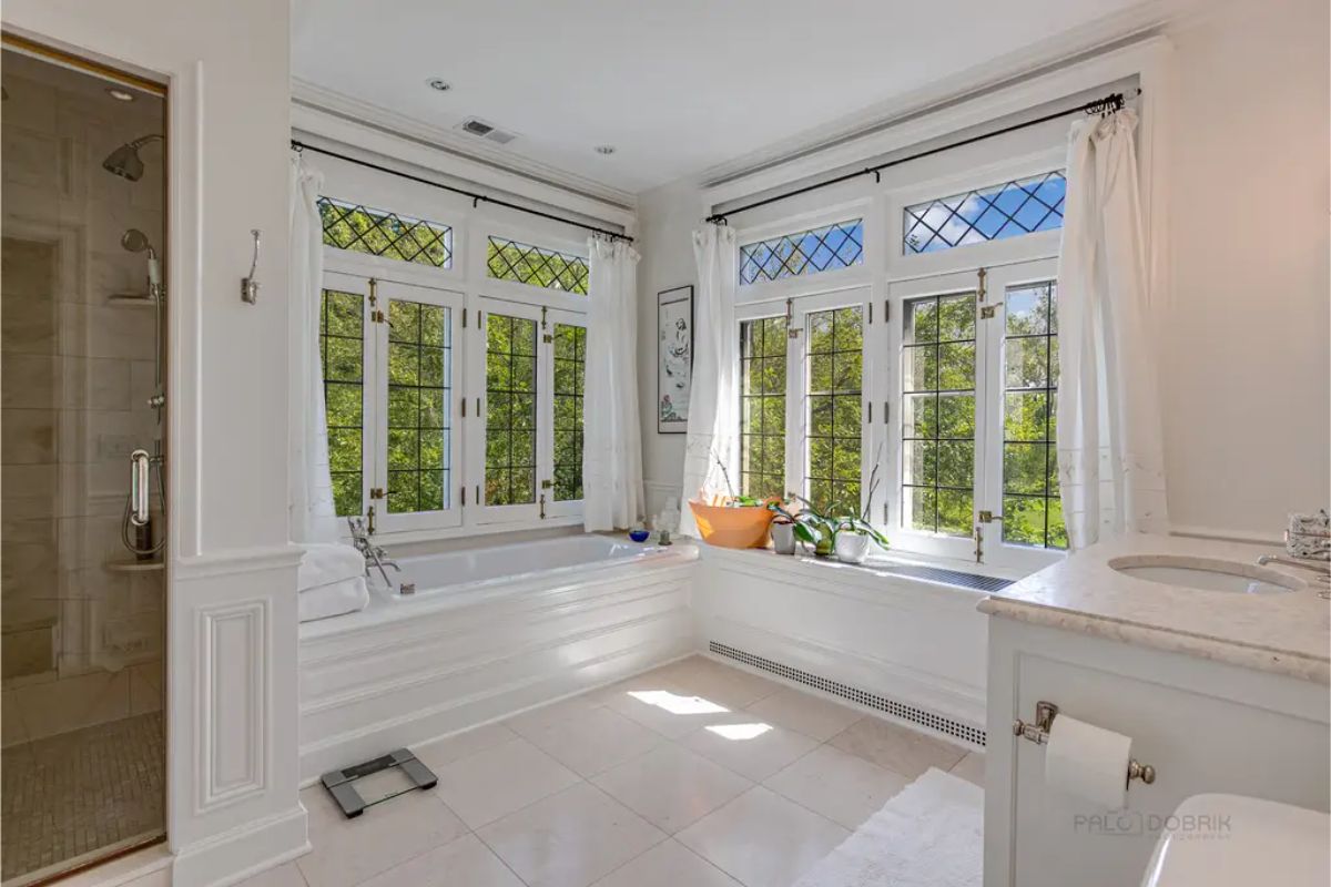 Bathroom with large windows featuring diamond-patterned panes and overlooking lush greenery.