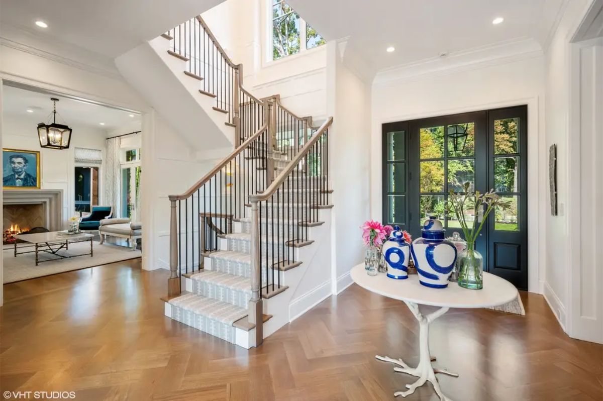 A bright, welcoming foyer featuring a grand staircase with wooden steps and metal railings, leading to the upper level.