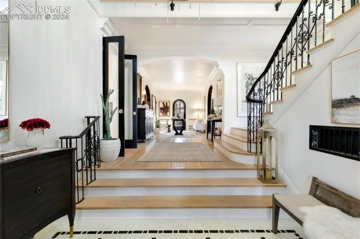 The grand entryway of this Italian Renaissance manor features a welcoming staircase adorned with custom wrought iron railings and light hardwood steps.
