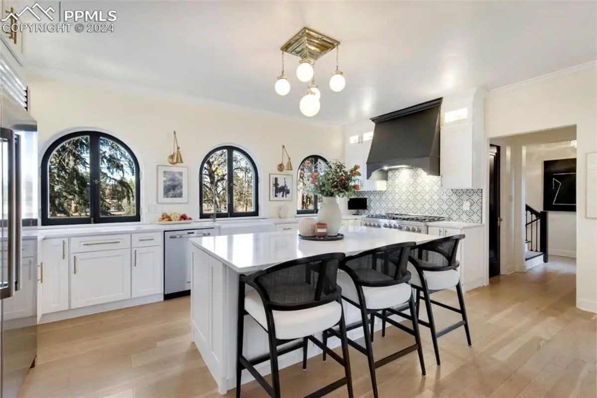 Sleek white cabinetry, a spacious central island with seating, and contemporary lighting fixtures.