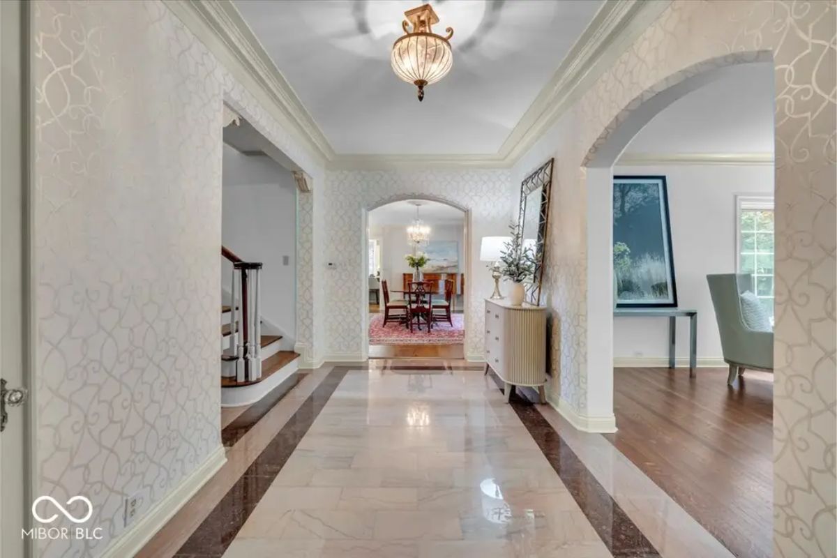 The grand foyer features polished marble flooring and leads to adjoining rooms through arched doorways, adding an elegant architectural touch.