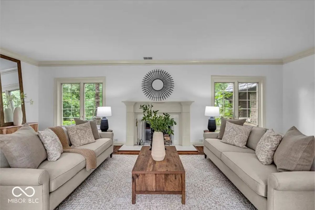 A spacious living room features neutral-toned sofas arranged around a rustic wooden coffee table.