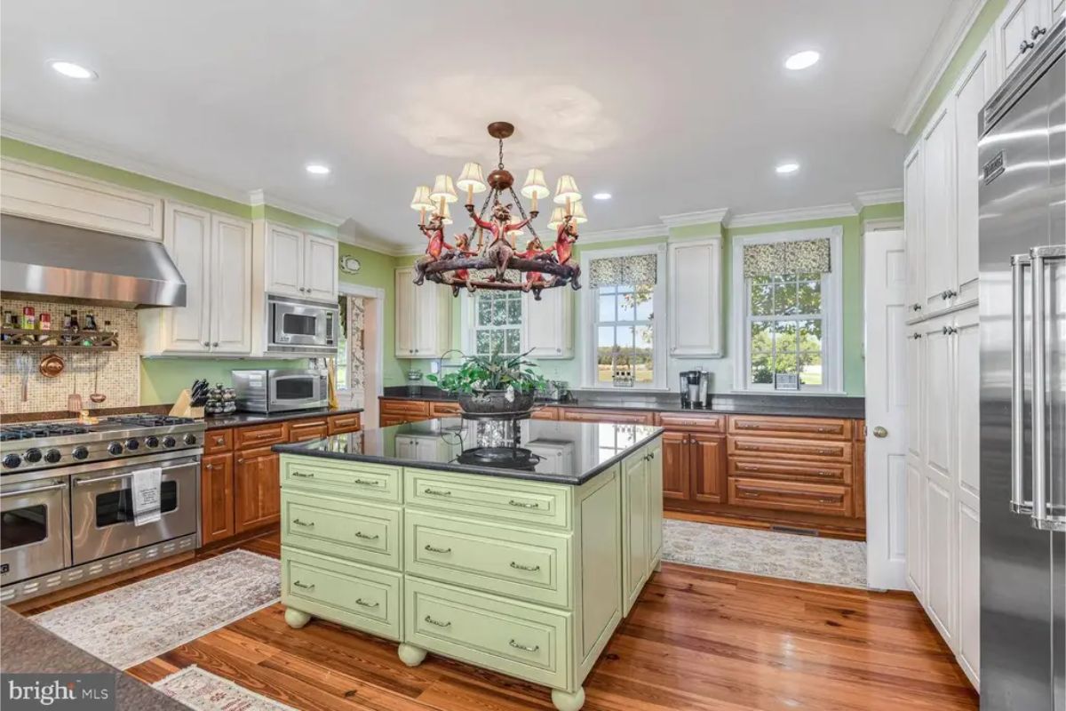 A central green island topped by a black countertop and surrounded by hardwood floors.
