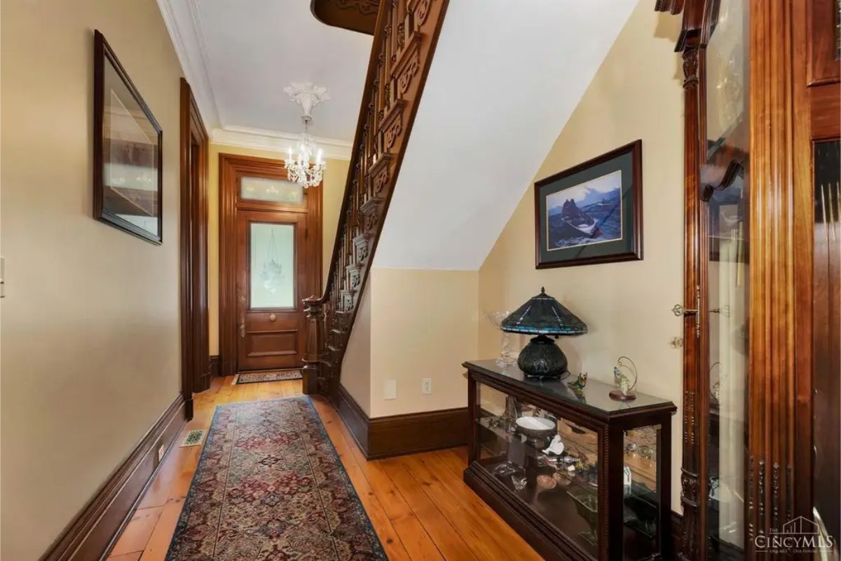 A warm and inviting hallway showcases intricate wood detailing on the staircase and door frames, reflecting the home's historic charm.