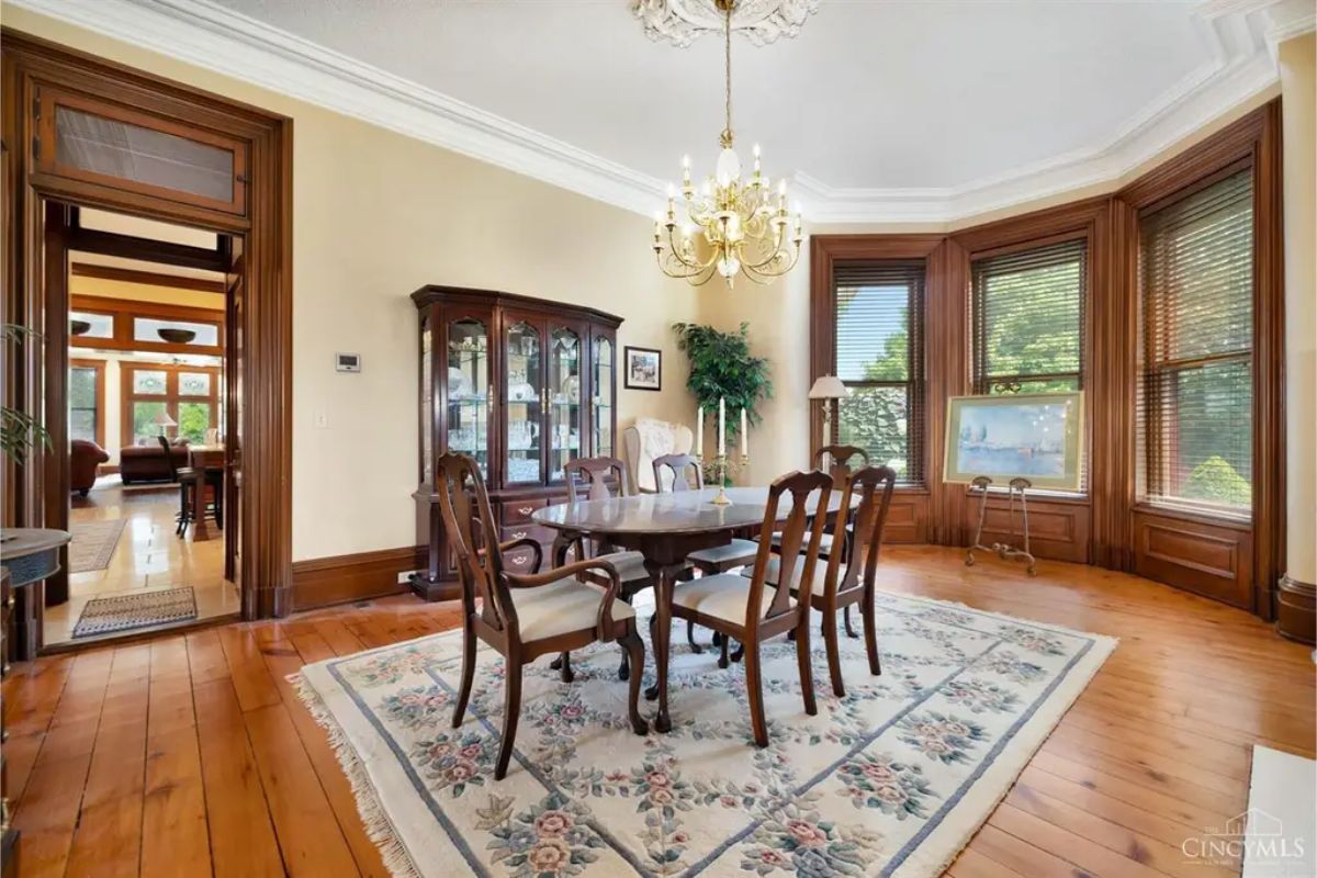 A formal dining room features a classic wooden table and chairs set on a floral-patterned area rug.