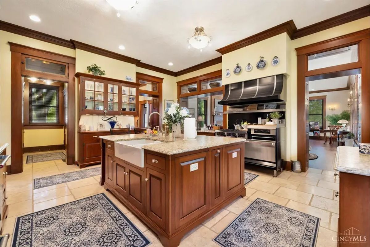 Kitchen boasts custom wood cabinetry, granite countertops, and a large central island with a farmhouse sink.
