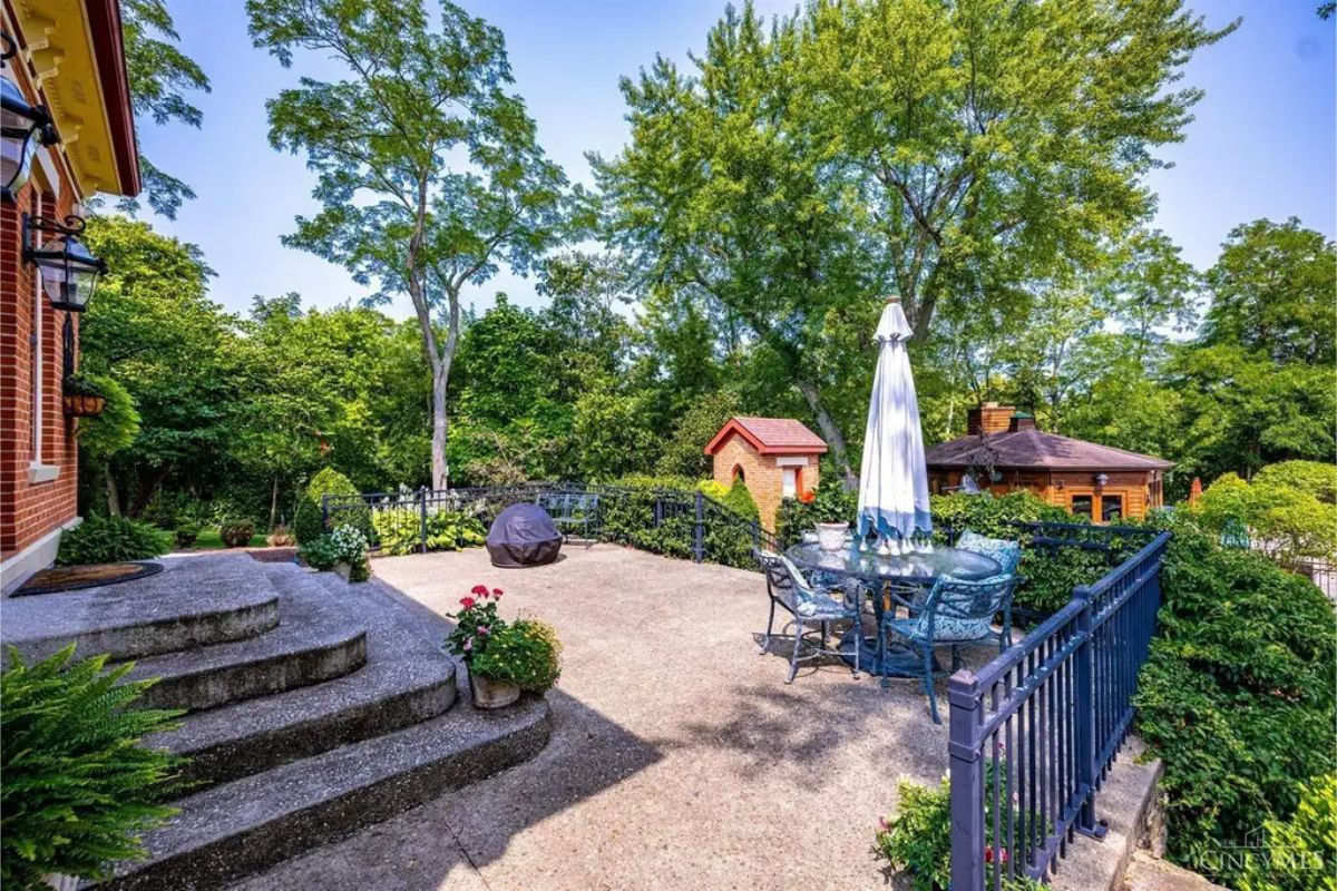 An outdoor patio offers ample space for relaxation and entertaining, surrounded by mature trees and vibrant greenery.