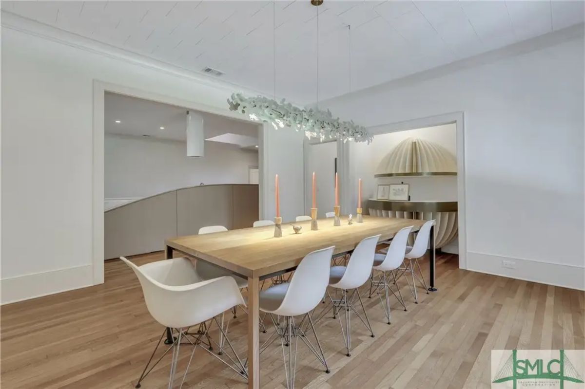 A long wooden table surrounded by white molded plastic chairs with metal legs.