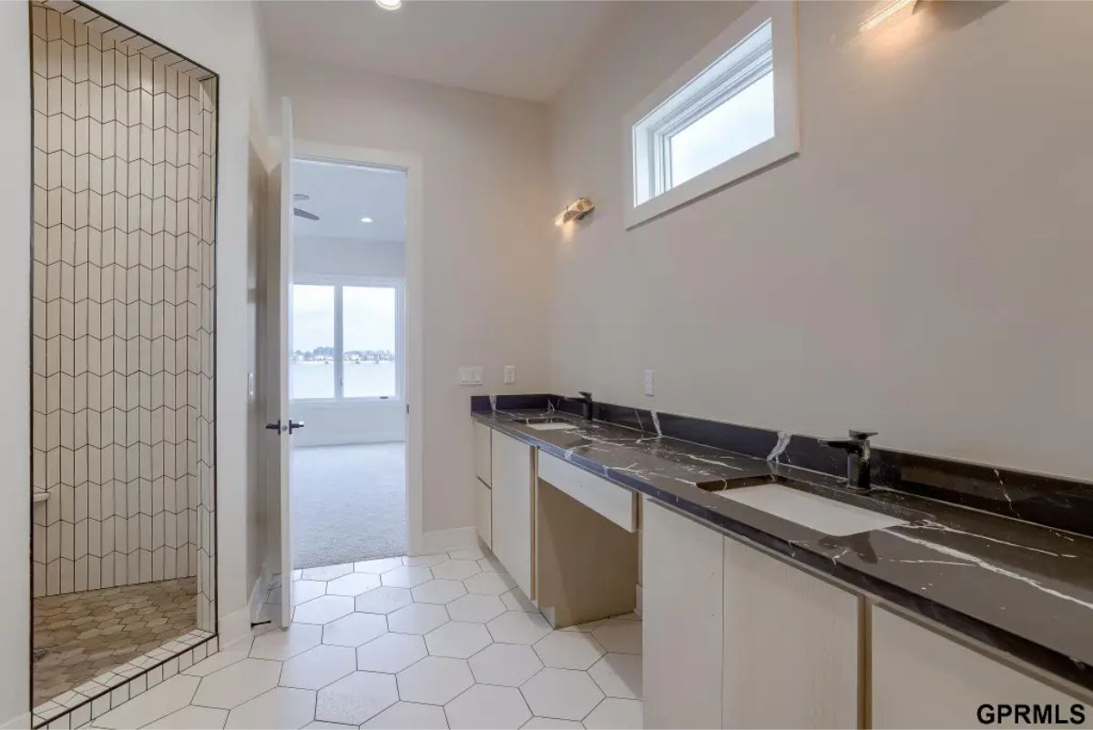 Bathroom with dual sinks set in a sleek black marble countertop, complemented by minimalist cabinetry.