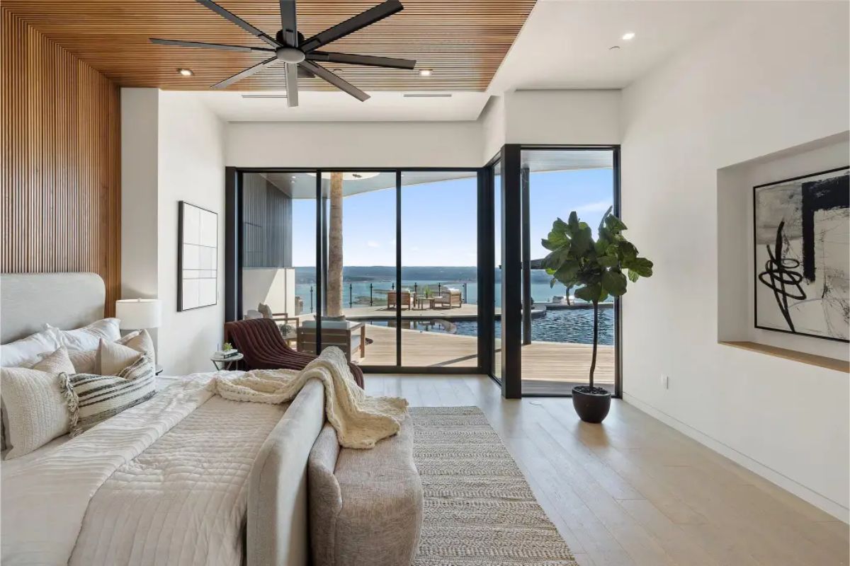 Elegant bedroom with a wood-paneled accent wall, large windows, and access to a terrace with a water view. 