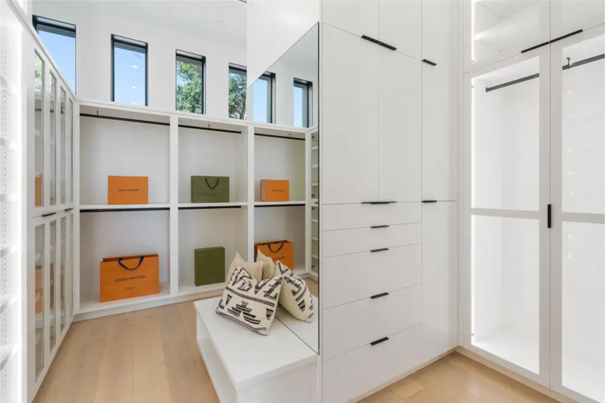 Walk-in closet with white cabinetry, glass display cases, and designer shopping bags. 