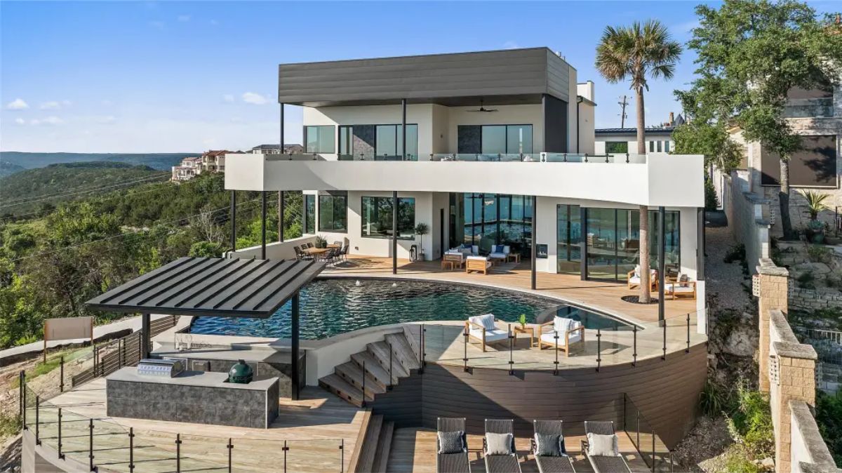 Contemporary multi-level house with a white exterior, black accents, and a rooftop balcony overlooking scenic surroundings. 