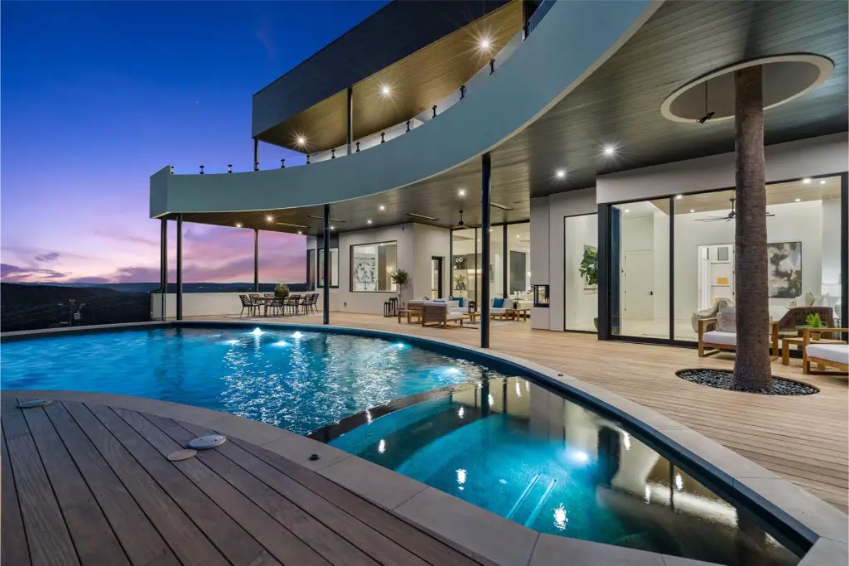 Curved infinity pool with a deck and patio area illuminated by blue lights, set against a modern architectural backdrop. 