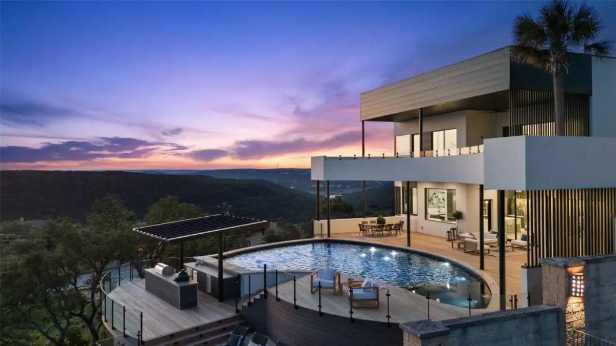 Luxury hilltop home features an expansive outdoor entertainment area with a panoramic sunset view and sleek design elements. 