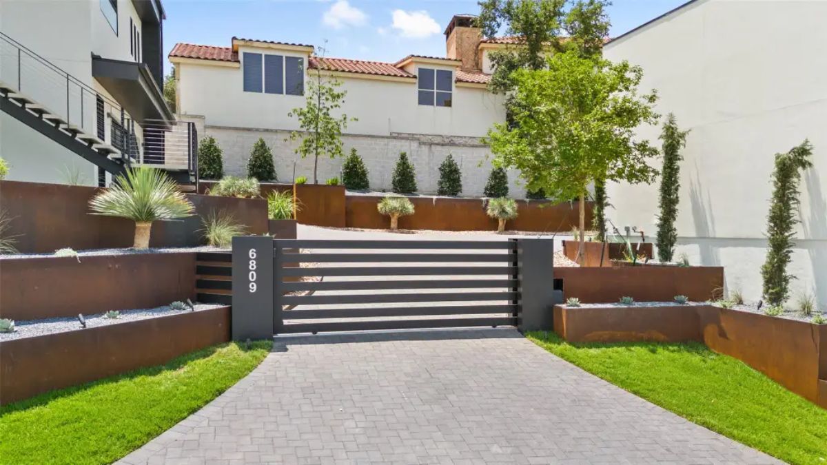 Gated driveway with landscaped retaining walls and greenery. 
