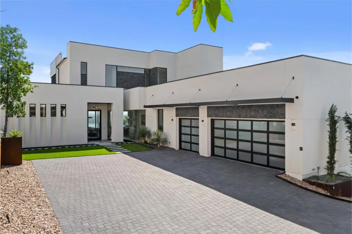 Minimalist driveway entrance with geometric landscaping, black-framed glass garage doors, and clean architectural lines. 