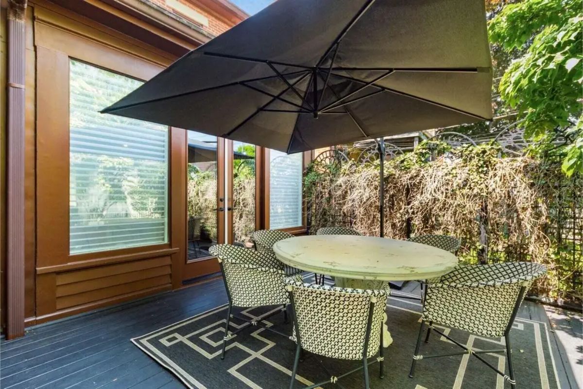 Round dining table surrounded by patterned chairs and shaded by a large black umbrella.