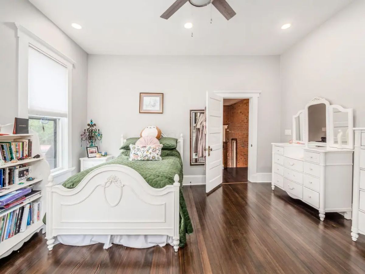 Cozy bedroom features elegant white furniture, including a detailed bed frame, matching dresser, and vanity, adding a timeless appeal.
