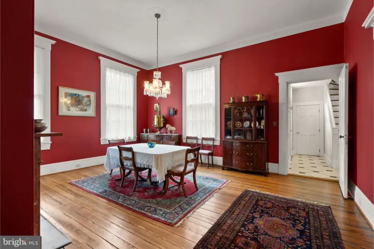 Dining room offers rich red walls accented by tall white-trimmed windows.
