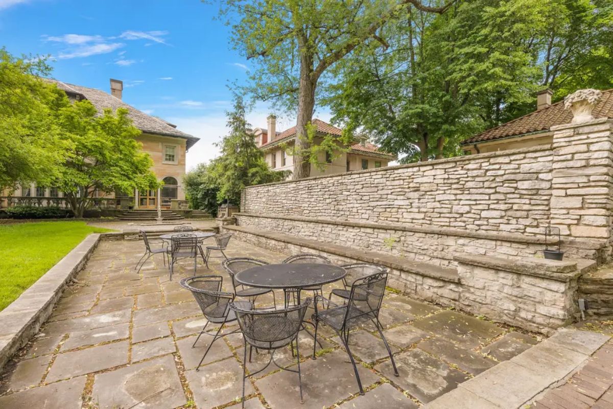 Stone patio is surrounded by lush greenery and historic architectural elements.