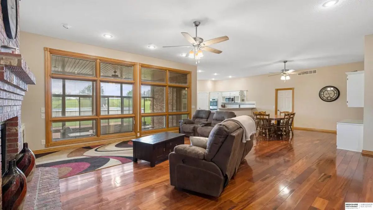 Living area with large floor-to-ceiling windows framed in wood, offering a view of an outdoor pool and greenery.