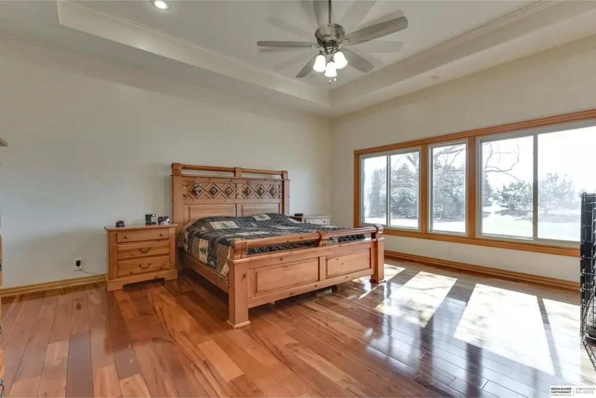 Large bedroom featuring polished wood flooring and a tray ceiling with a fan for added comfort.