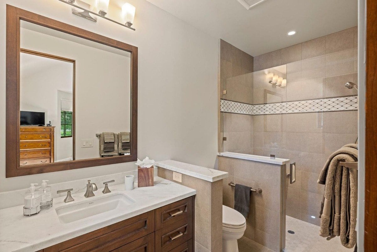 Bathroom features a marble-topped vanity with a wood-framed mirror and a glass-enclosed shower with patterned tile detailing.
