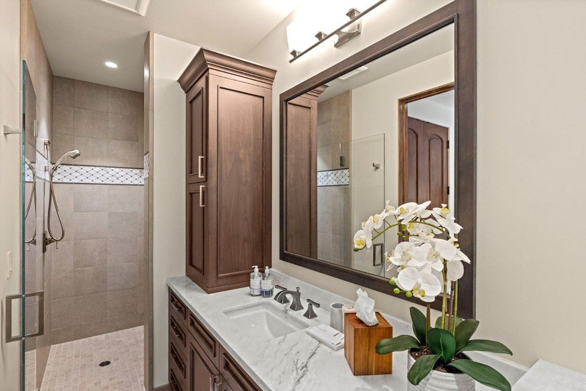 Bathroom design features a modern vanity with a marble countertop, a large framed mirror, and a glass-enclosed shower.