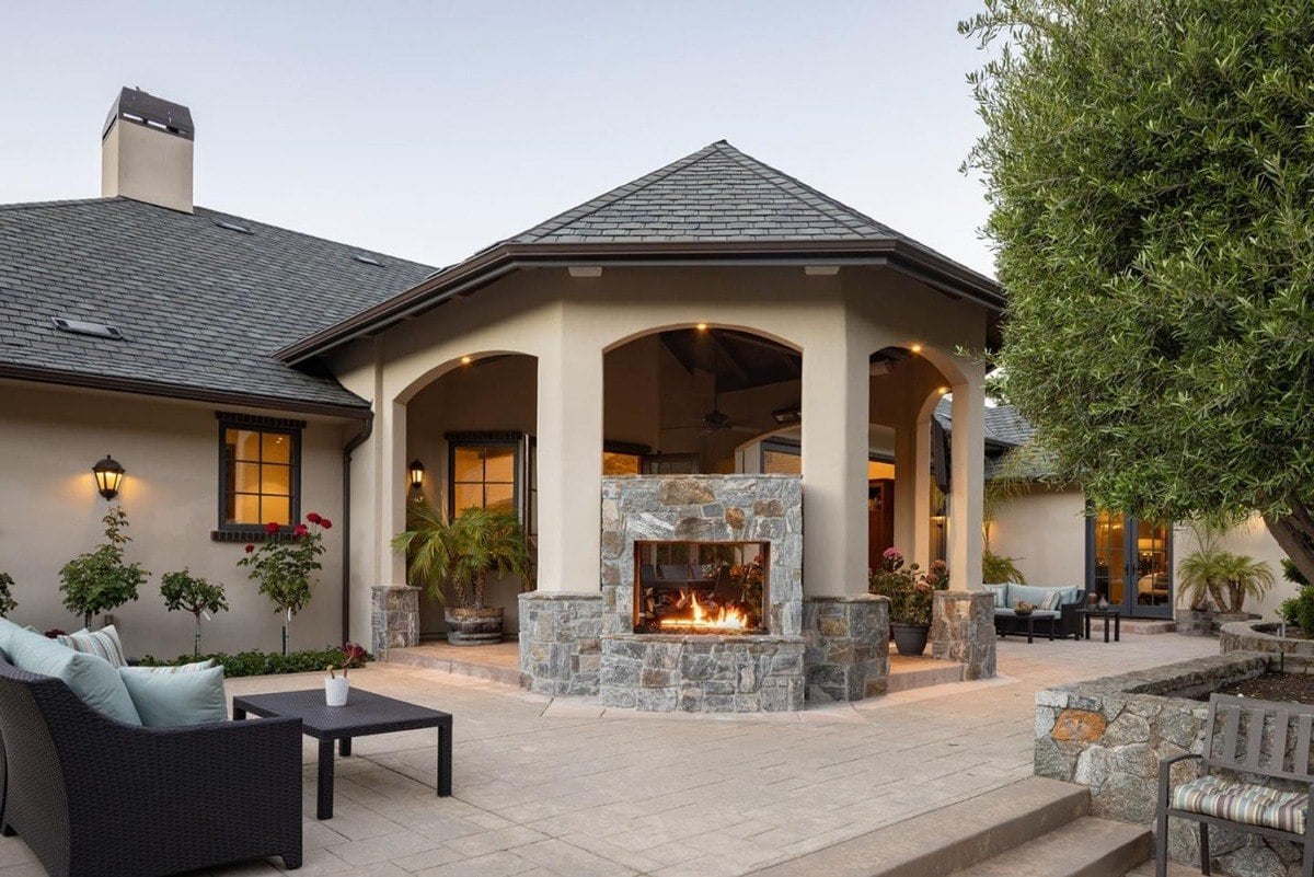 Covered terrace features a stone fireplace with cozy seating and floral accents.