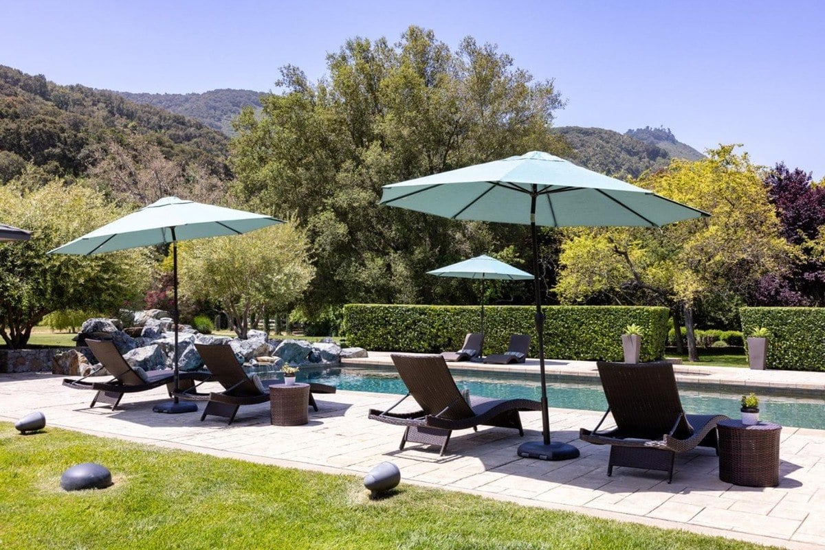 Poolside view highlights lounge chairs under wide umbrellas with a backdrop of trees and hills.