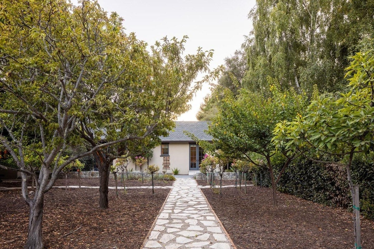 Stone pathway lined with fruit trees leads to a charming garden structure.