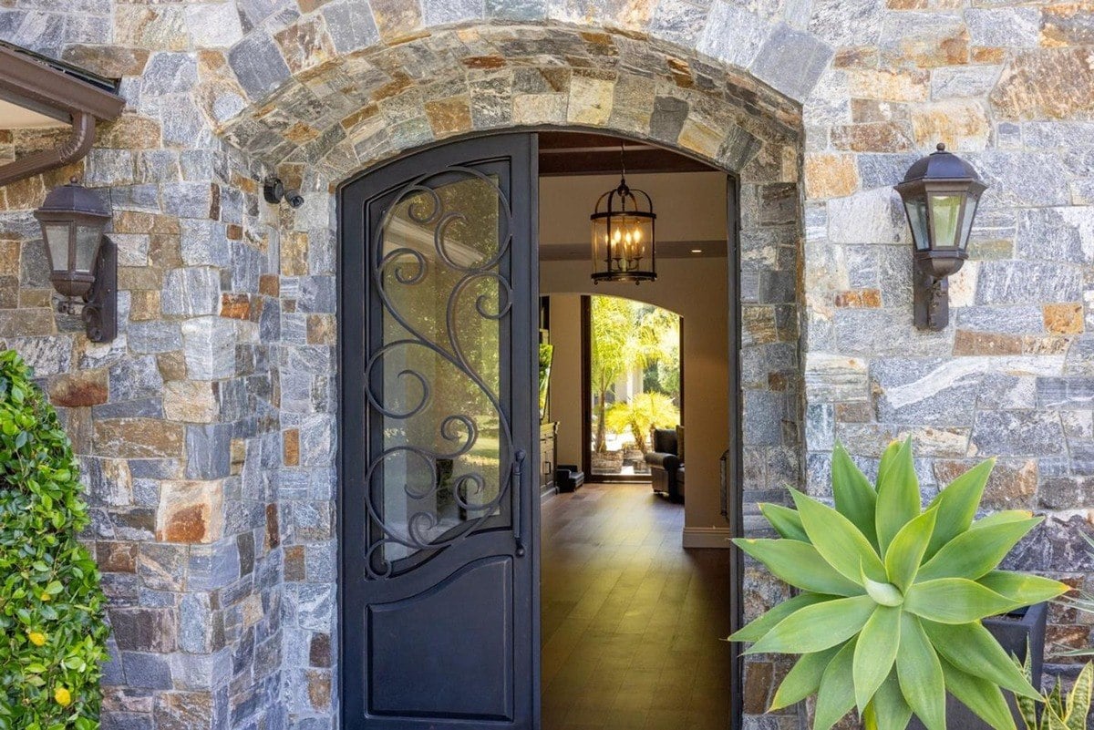 Wrought iron front door embedded within an arched stone frame, providing a glimpse into the bright interior.