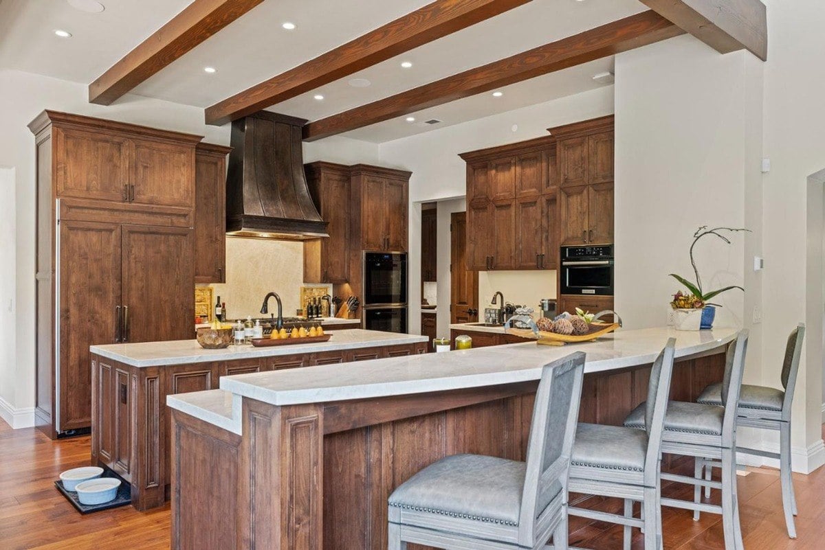 Elegant kitchen with rich wooden cabinetry, exposed ceiling beams, and a large center island.