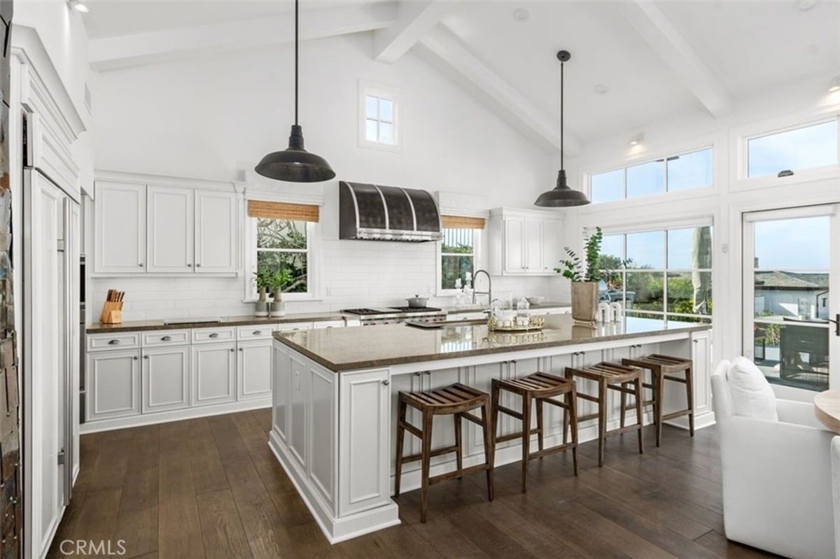 Spacious kitchen with white cabinets, a large island with seating, and multiple windows allowing natural light.
