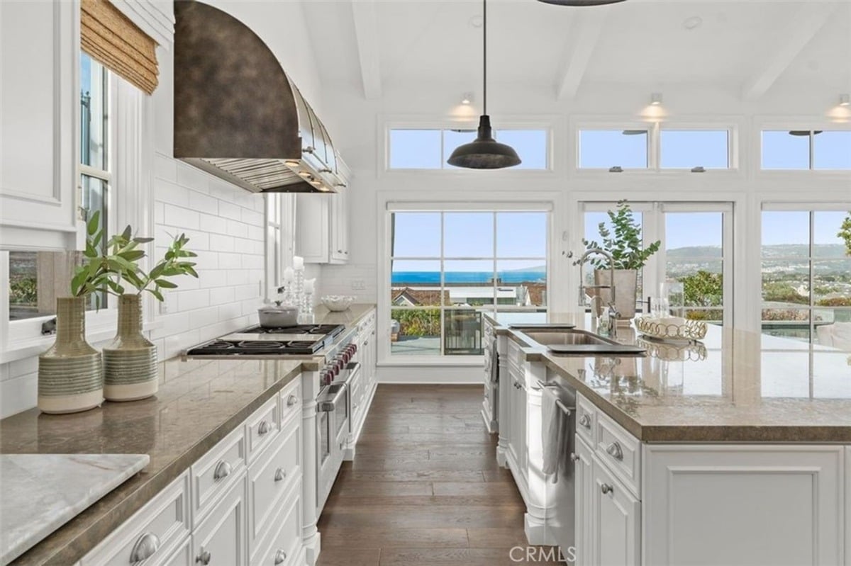 Kitchen layout highlighting a large oven range, white cabinetry, and a panoramic view of the ocean through expansive windows.