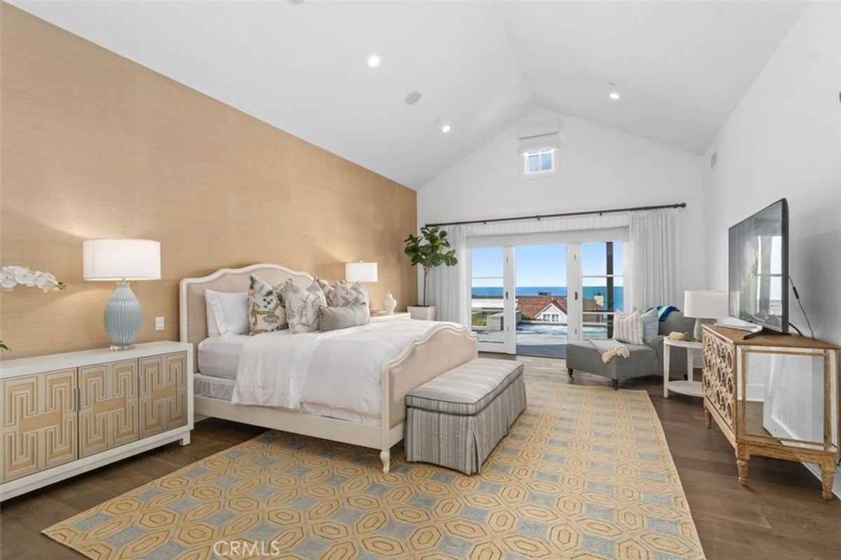 Primary bedroom with a vaulted ceiling, a light-toned accent wall, and a seating area overlooking ocean views.