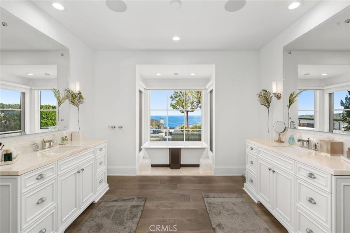 Bathroom featuring dual vanities, a central soaking tub, and a view of the ocean through large windows.