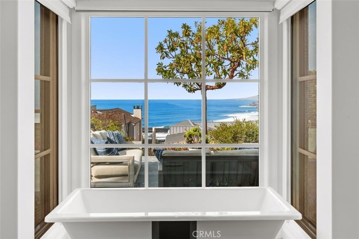 Close-up of a soaking tub with a framed view of the ocean and outdoor seating area through a large window.
