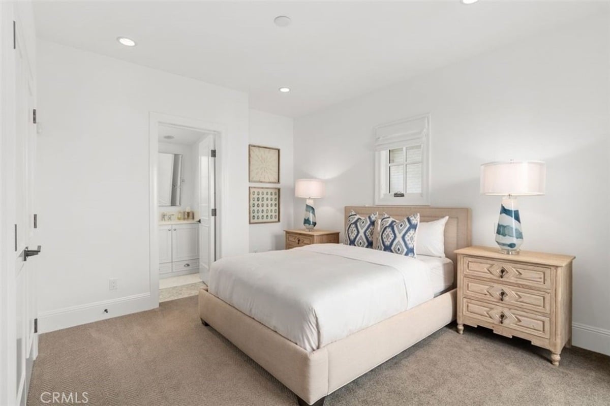 Guest bedroom with a neutral color scheme, twin bedside tables, and an attached bathroom visible through an open door.