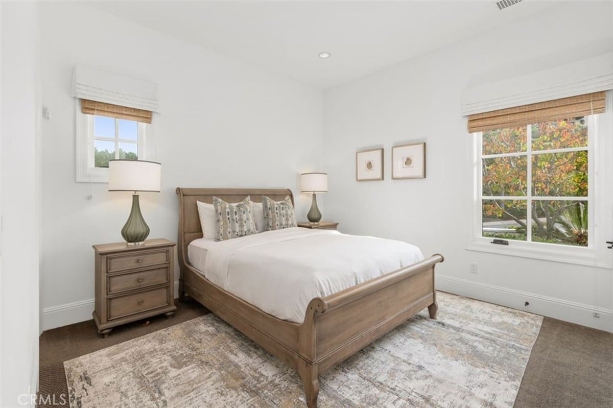 Spacious bedroom with a wooden bed frame, neutral decor, and large windows allowing natural light.