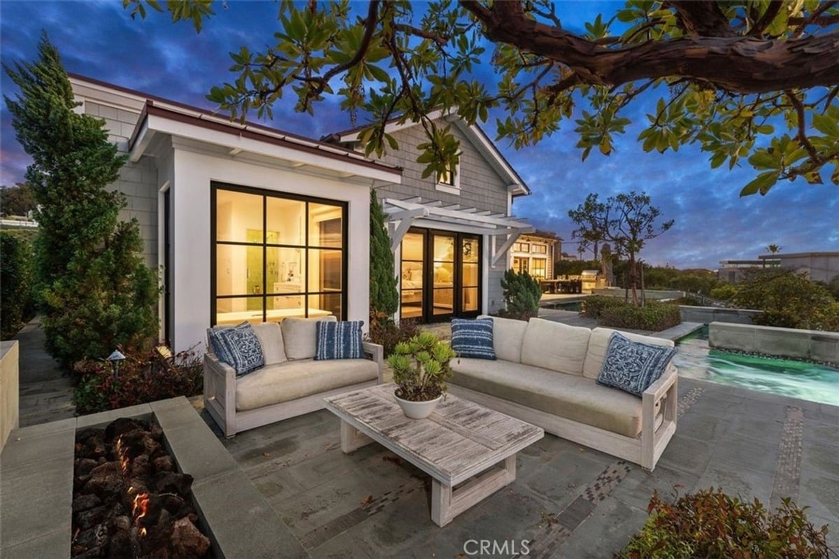 Outdoor seating arrangement with sofas, a fire pit, and lush landscaping in a serene setting.