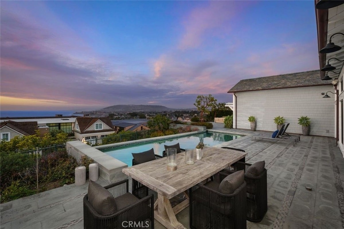 Stunning sunset view over a pool area with dining furniture and panoramic coastal scenery.