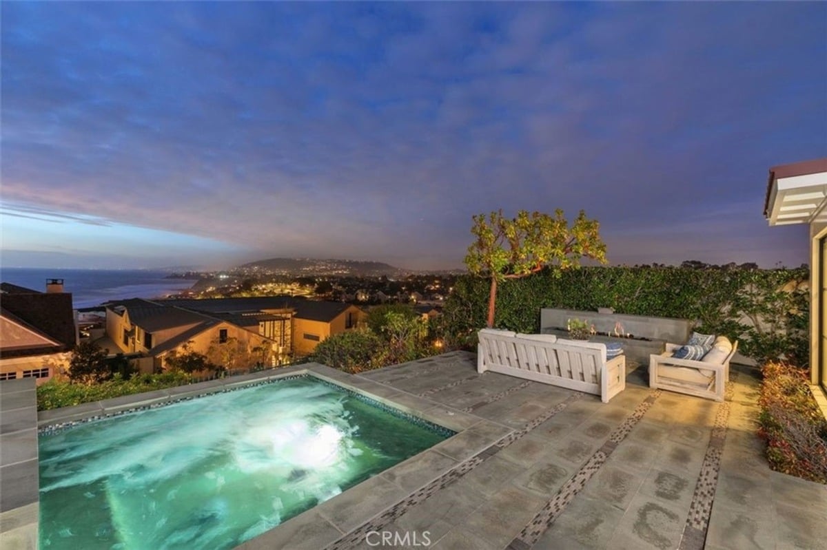 Outdoor lounge area featuring a hot tub, white sofas, and an expansive ocean view.