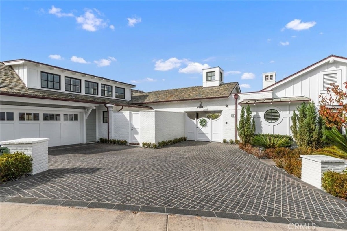 Modern driveway leading to a white-painted residence with a circular window and greenery accents.